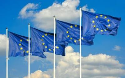 Fire EU-flagg som vaier i vinden mot en blå himmel med skyer